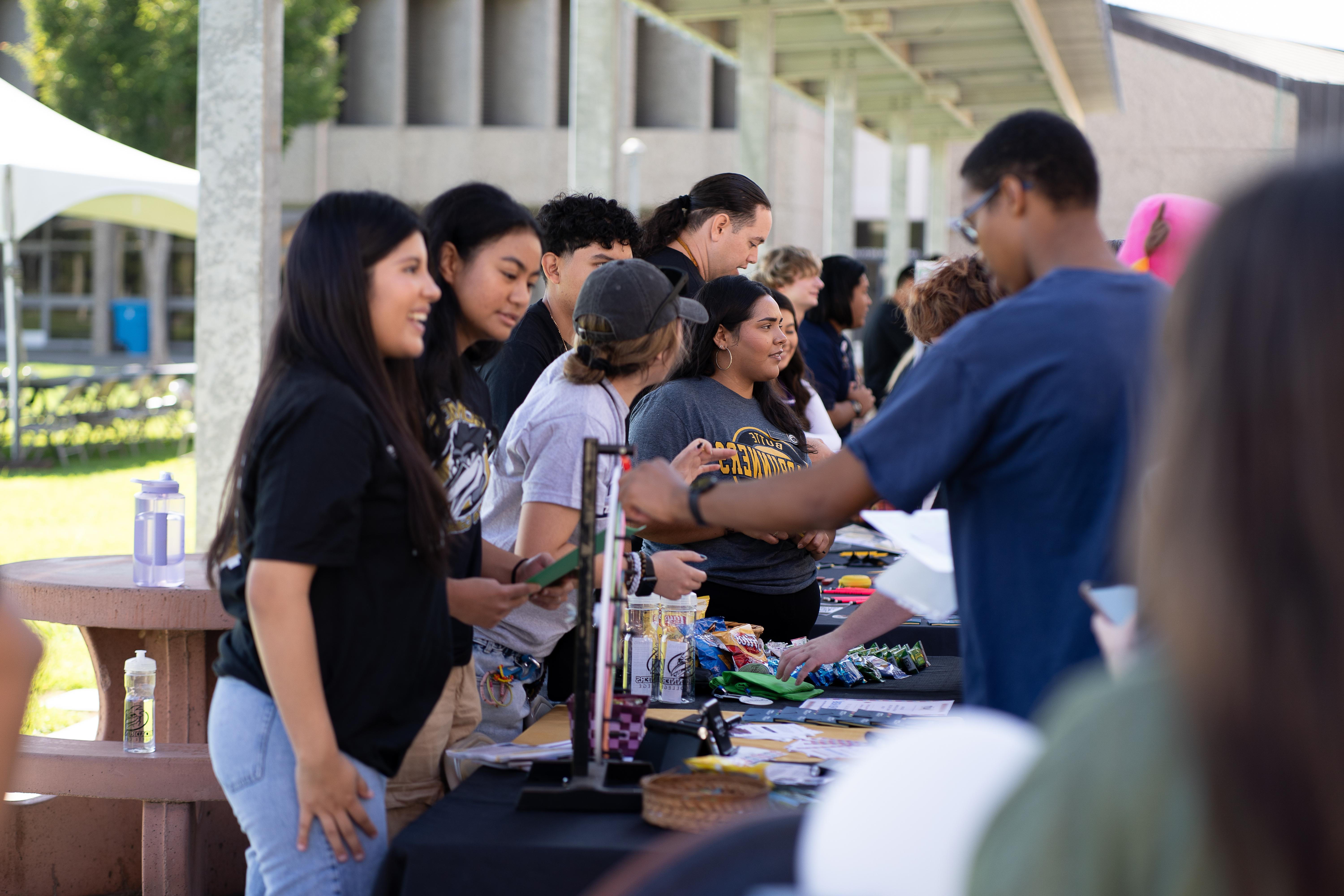 a group of students and staff members are shown interacting at information booths on campus. with 